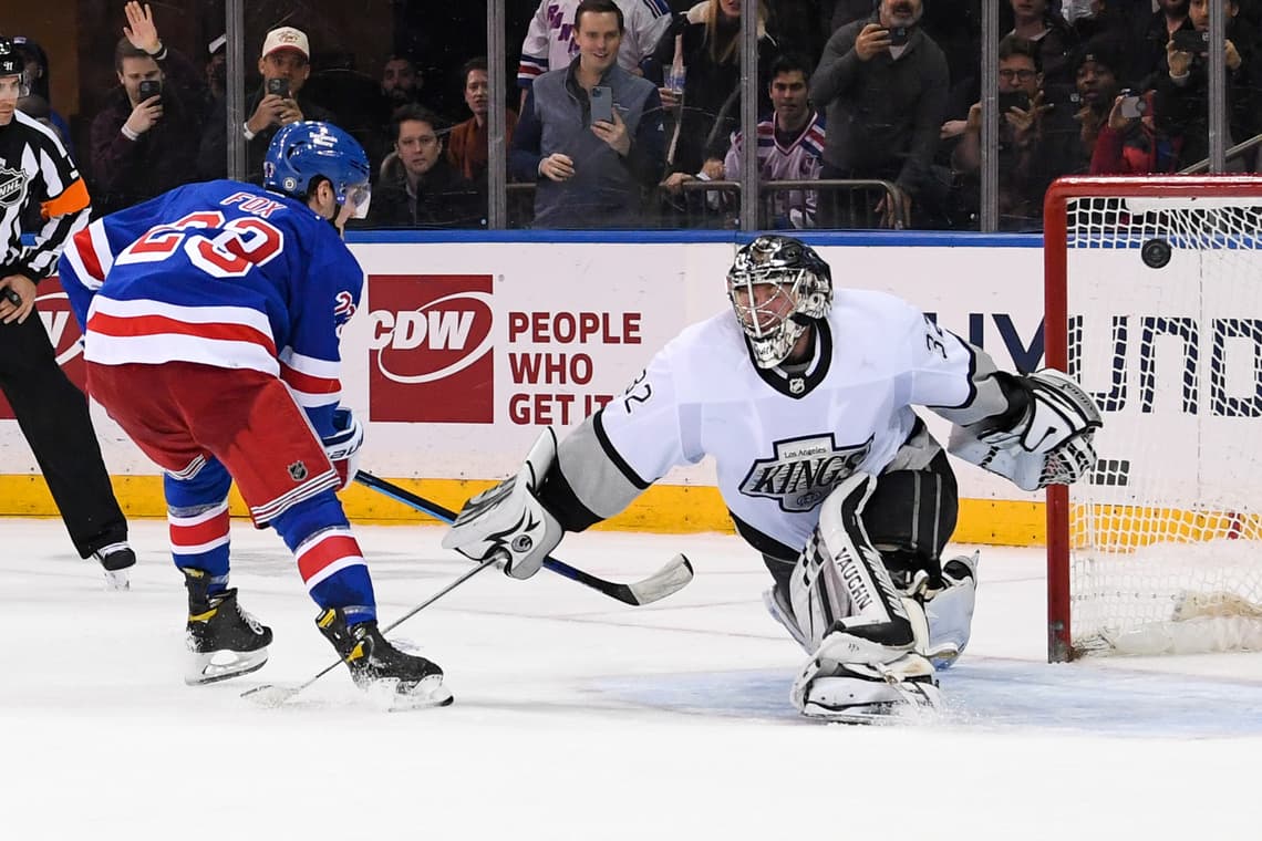Goaltender in white Kings jersey defending net against Rangers player in blue jersey