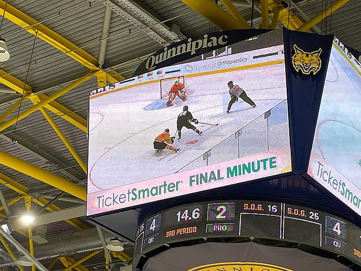 Hockey game scoreboard displaying final minute action with player in black jersey and goalie in red