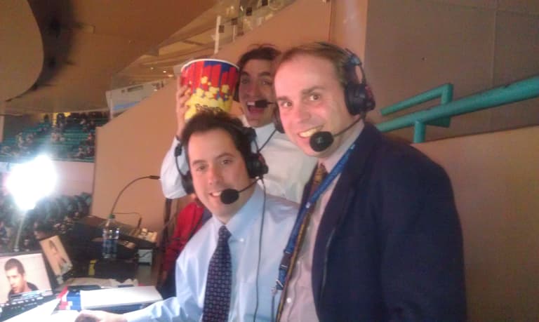 Three men wearing headsets at a broadcasting booth during a hockey game