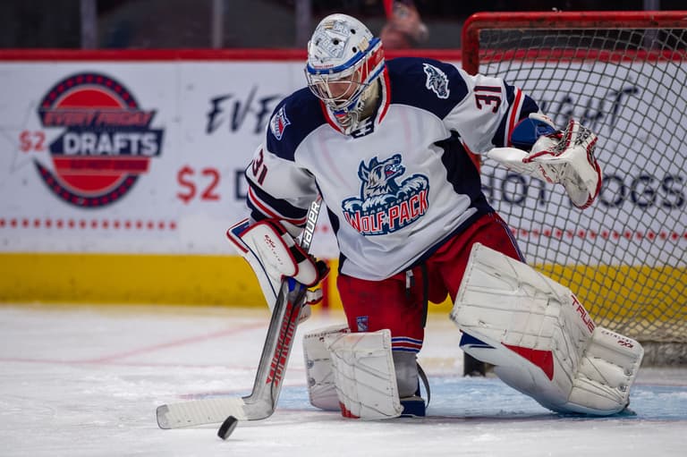 Wolf Pack goalie in white jersey making a save during game