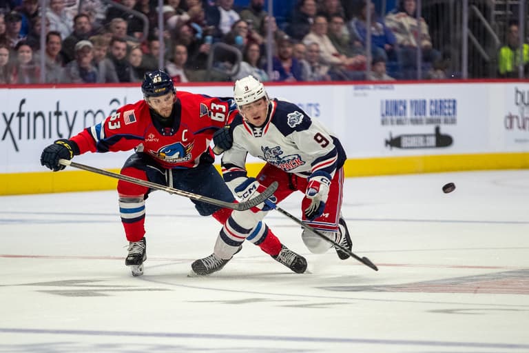 Hockey player in white jersey competing for puck against red-jerseyed opponent during game
