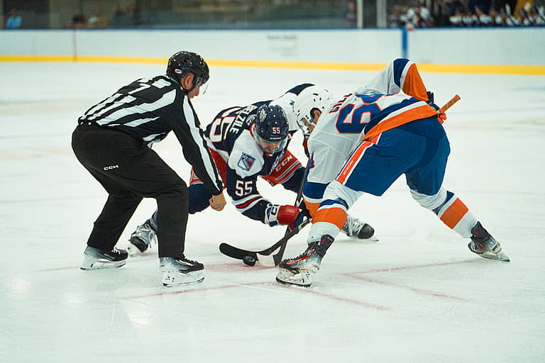 Referee dropping puck for face-off between two hockey players during practice