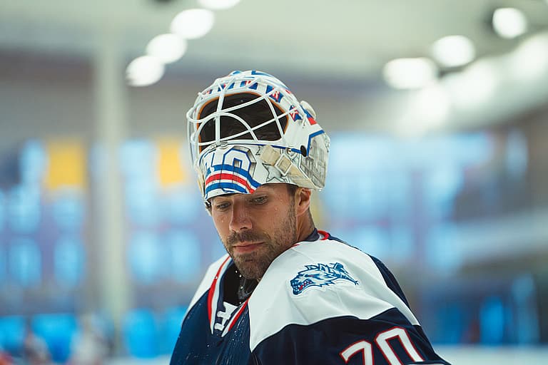 Hockey goaltender in white mask and navy jersey with shark logo during game