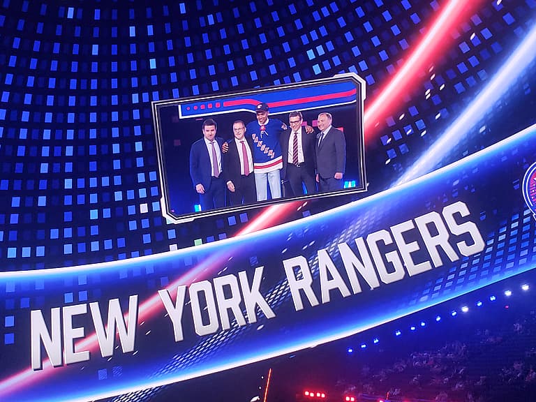 Five men in business attire posing with a Rangers player at a sporting event