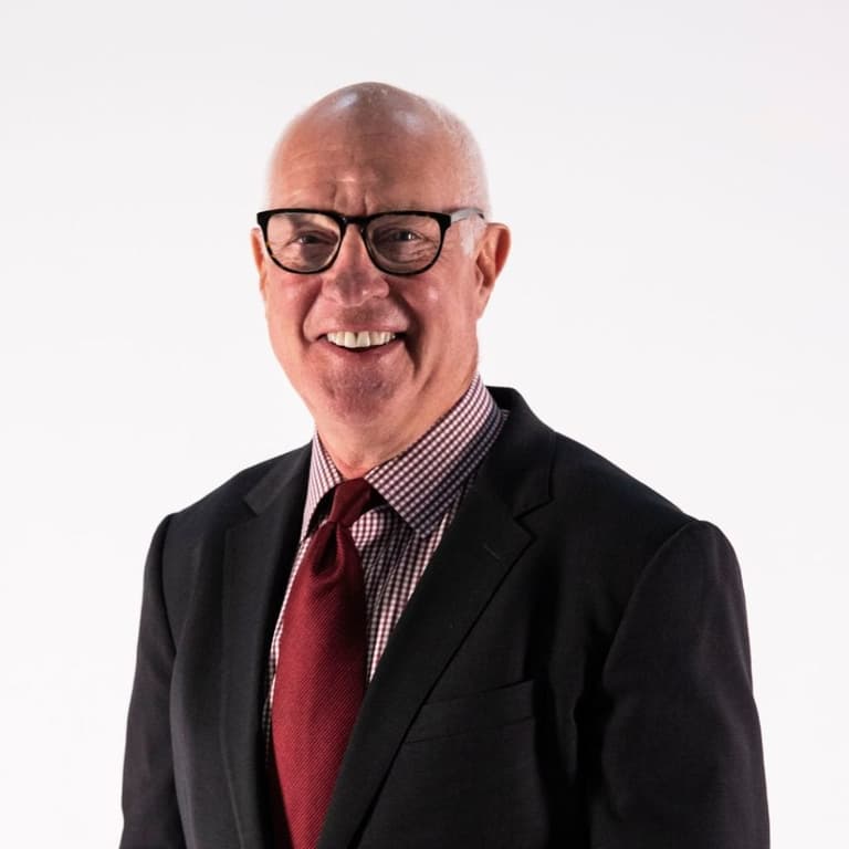 Professional headshot of a man wearing glasses, black blazer, checkered shirt, and maroon tie