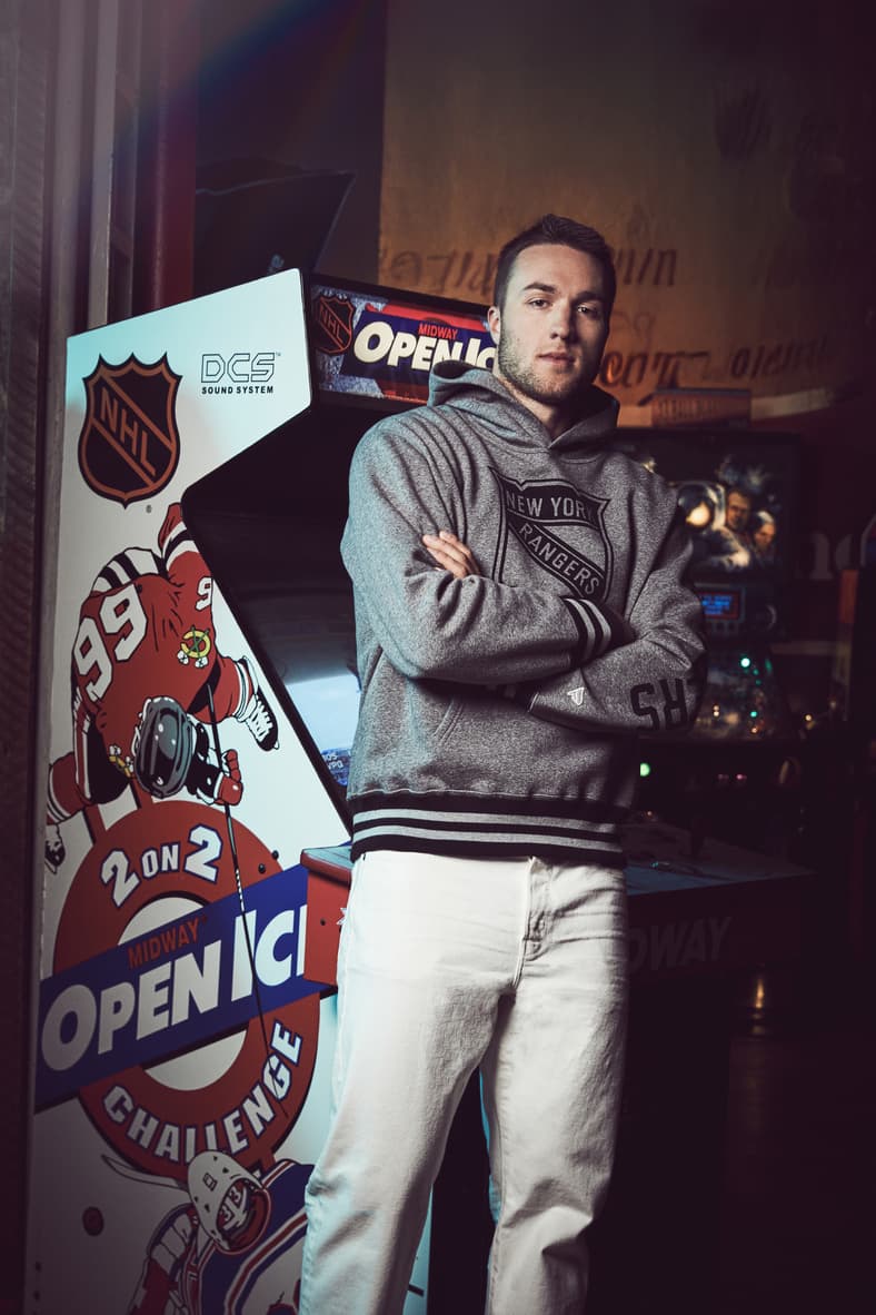 Man in New York Rangers hoodie standing beside NHL arcade game machine