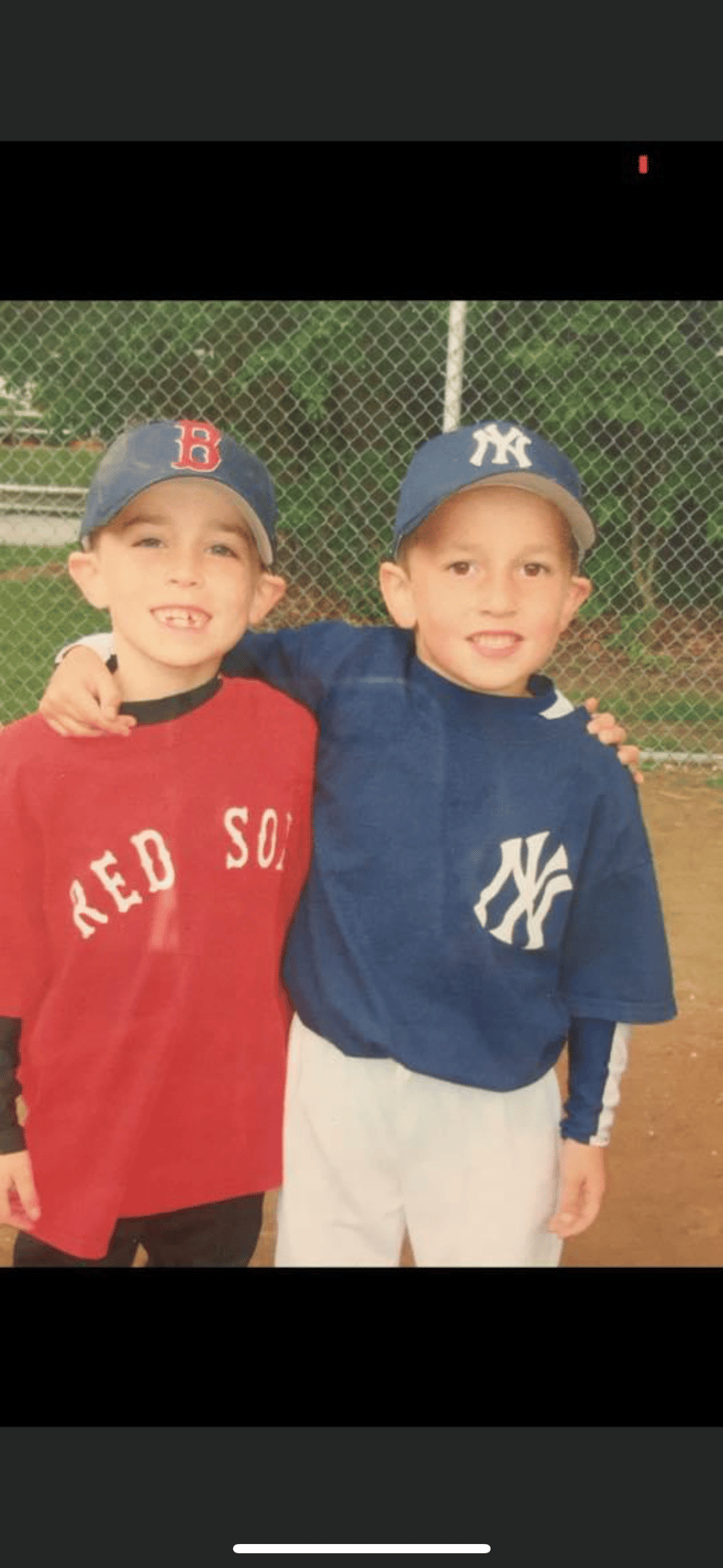 Two young boys in Red Sox and Yankees uniforms at a baseball field