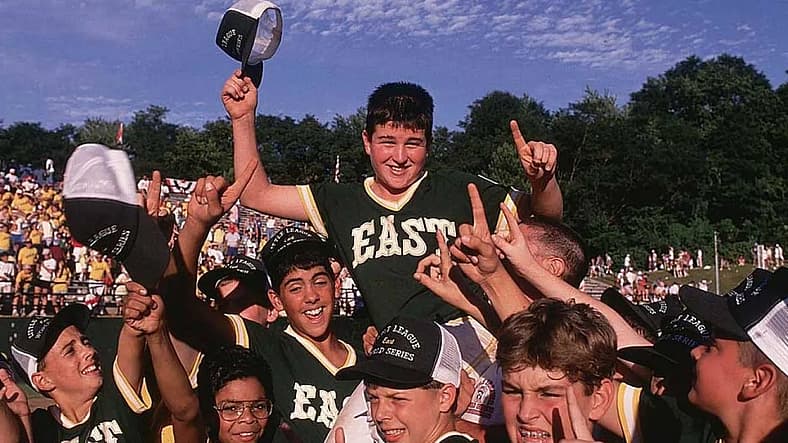 Young baseball player holds trophy while celebrating with teammates at Little League World Series