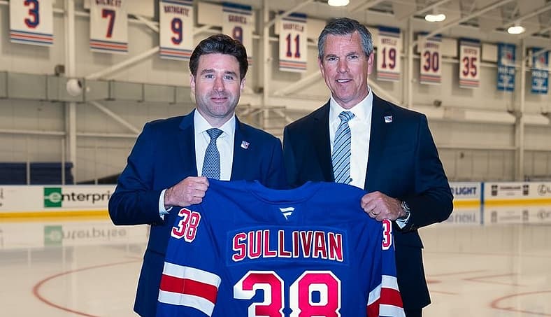 Two men in business suits holding a Sullivan #38 Rangers jersey in an ice hockey arena