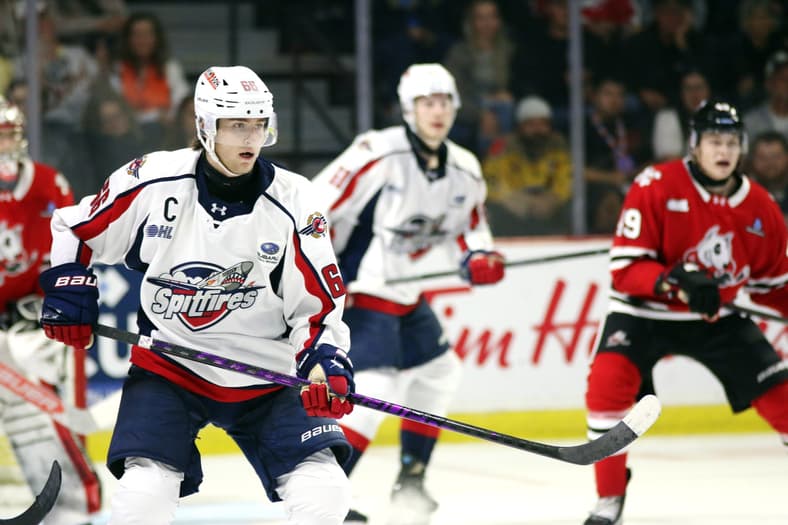 Hockey player wearing Spitfires white jersey with captain's C skates with puck during game