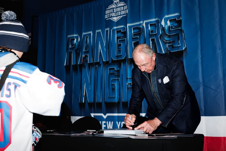 Man signing autographs at Rangers event with blue backdrop