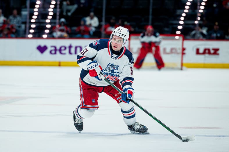 Hockey player in Rangers uniform skating with puck during game