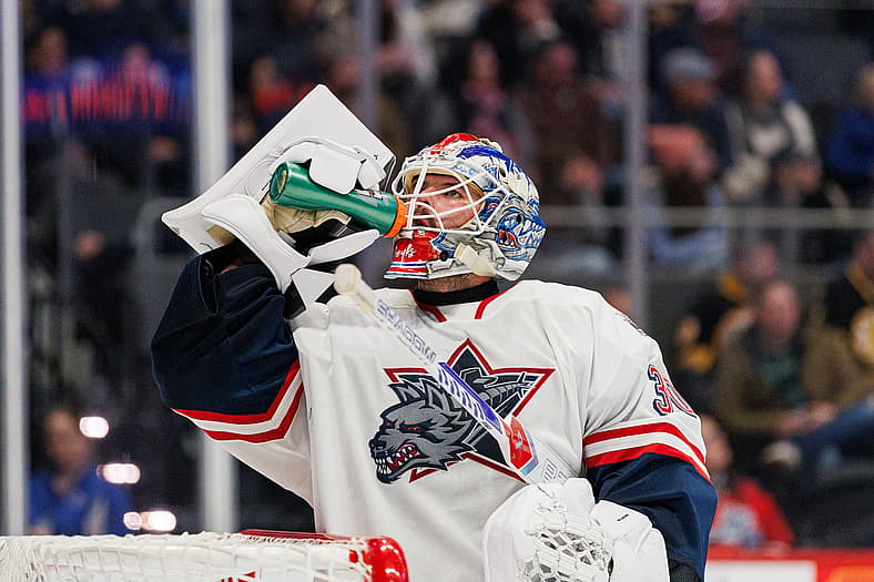 Goaltender in white Hartford Wolf Pack jersey drinking from water bottle during game