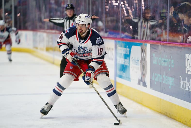 Hockey player wearing Hartford Wolf Pack uniform number 18 with puck during game