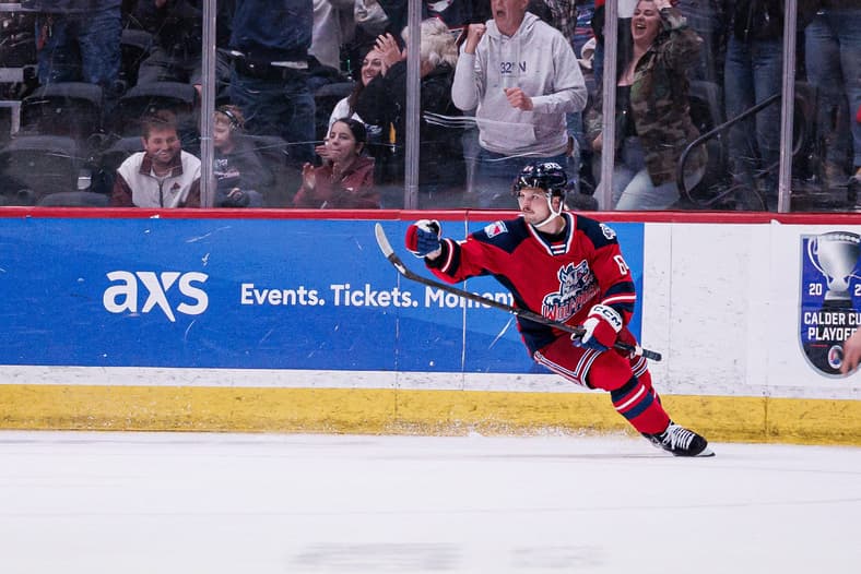 Hartford Wolf Pack player in red jersey skating along the boards during a playoff game
